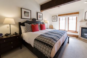 A cozy bedroom with a large bed, a fireplace, and a window.