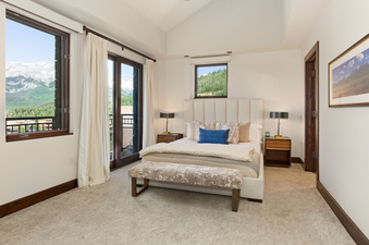 The bedroom in Lumiere Three Bedroom Penthouse features a king-sized bed with a plush headboard and a plush throw blanket, along with a  comfy bench at the foot of the bed.  The room also boasts a view of the mountains from a large window and french doors