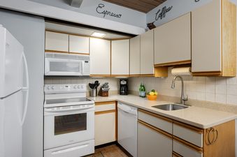 A bright and tidy kitchen featuring white appliances, light wood cabinetry, and a subway tile backsplash.