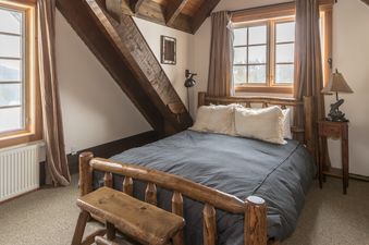 A cozy bedroom in Camp Arrowhead Cabin with a rustic wooden bed, two windows, and warm lighting.