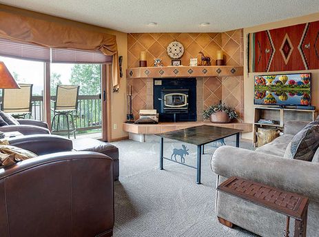 The spacious living room at The Ranch at Steamboat RA501 features plush seating, a tile fireplace, and a large window overlooking the natural landscape.