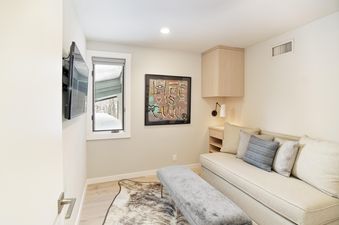A cozy bedroom at Tamarack 04 featuring a daybed with pillows, a wall-mounted TV, artwork, a cowhide rug, and a window showcasing a snowy outdoor view.
