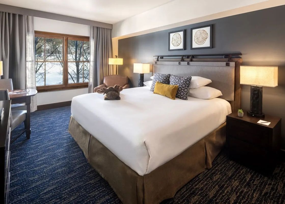 Cozy bedroom in the Teton Mountain Lodge and Spa Sundance Junior Suite featuring a king bed and snowy window views.