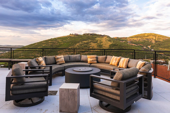 An inviting outdoor patio at Kings Crown Hideaway with a circular fire pit and comfortable seating, set against a backdrop of rolling green mountains under a dramatic sky.
