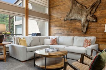 A spacious living room with a large L-shaped sofa, a round coffee table, and a wooden accent wall with an animal hide.