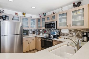 A modern kitchen with stainless steel appliances, light wood cabinets with frosted glass, and rooster decorations.