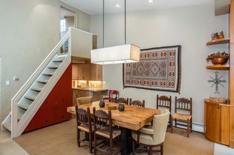 A spacious dining area with a large wooden table and chairs, a kitchen counter with a sink, and a staircase leading upstairs.