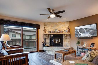 A cozy living room at Ranch at Steamboat RA401 featuring a fireplace, a television, and a balcony access.