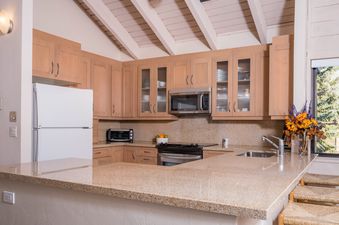 A kitchen with wood cabinets and a breakfast bar with a view of the trees outside.