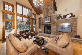 A cozy living room in Last Nickel Lodge with a stone fireplace, comfortable sofas, and large windows offering a snowy winter view.