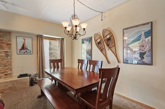 A wooden dining table with six chairs and a bench in a ski-themed dining room with two vintage ski posters and snowshoes on the wall.