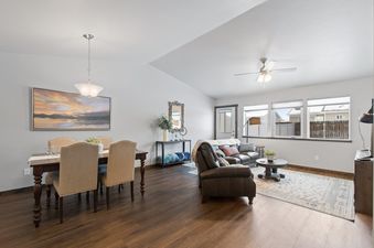 An expansive open concept living and dining area at Destiny Cove features elegant furnishings, a warm color palette, and abundant natural light from large windows showcasing a snowy neighborhood view.