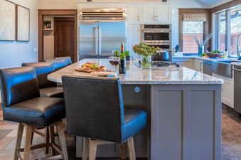 The kitchen at the Abode at Sage Springs features a large island with three bar stools, a modern chandelier, and stainless steel appliances.