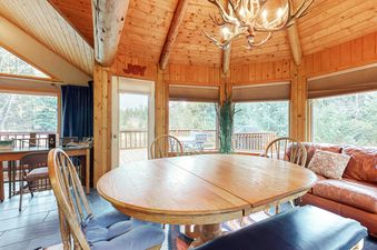 The dining area in the Lone Walker Home features a rustic wooden table with seating for guests and large windows that provide a beautiful view of the outdoor surroundings.