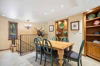 A wooden dining table with green chairs and a mounted elk head on the wall in a home.