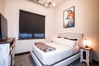The bedroom at 2nd Street Lofts 302 is warm and inviting, featuring a comfortable bed, bedside table with lamp, and an artwork of a fox.