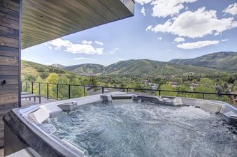 A close-up view of the outdoor hot tub at the Nine Peaks, filled with bubbling water, set against a stunning backdrop of green mountains and a clear sky.