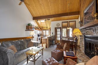 An inviting and open-concept living area with a stone fireplace, comfortable seating, a dining space, and a well-equipped kitchen.