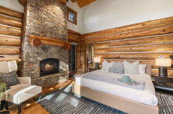 A rustic bedroom with a large stone fireplace, log walls, and a king bed at Timber Ridge at Jackson Hole.