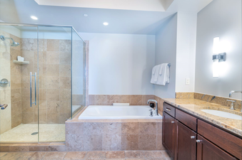 Lumiere Studio Deluxe bathroom, with a large bathtub, a walk-in shower, a double vanity with a marble countertop, and wood cabinetry.