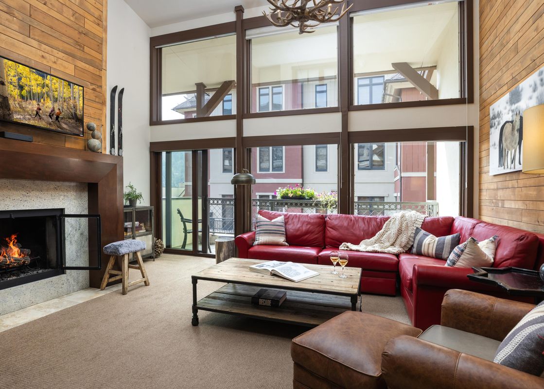 The welcoming living area at Montaneros 421 with a red sectional sofa, stone fireplace, and floor-to-ceiling windows.