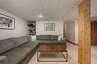 The comfortable living area at 980 Mulligan features a large L-shaped sectional sofa and a wooden coffee table, set against a backdrop of white walls and a carpeted floor, with artwork adorning the walls.