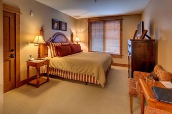 A hotel room with a king sized bed, wooden furniture and a large window with blinds.