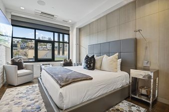 A modern bedroom with a large bed, stylish furniture, and a window offering a view of a hillside neighborhood.