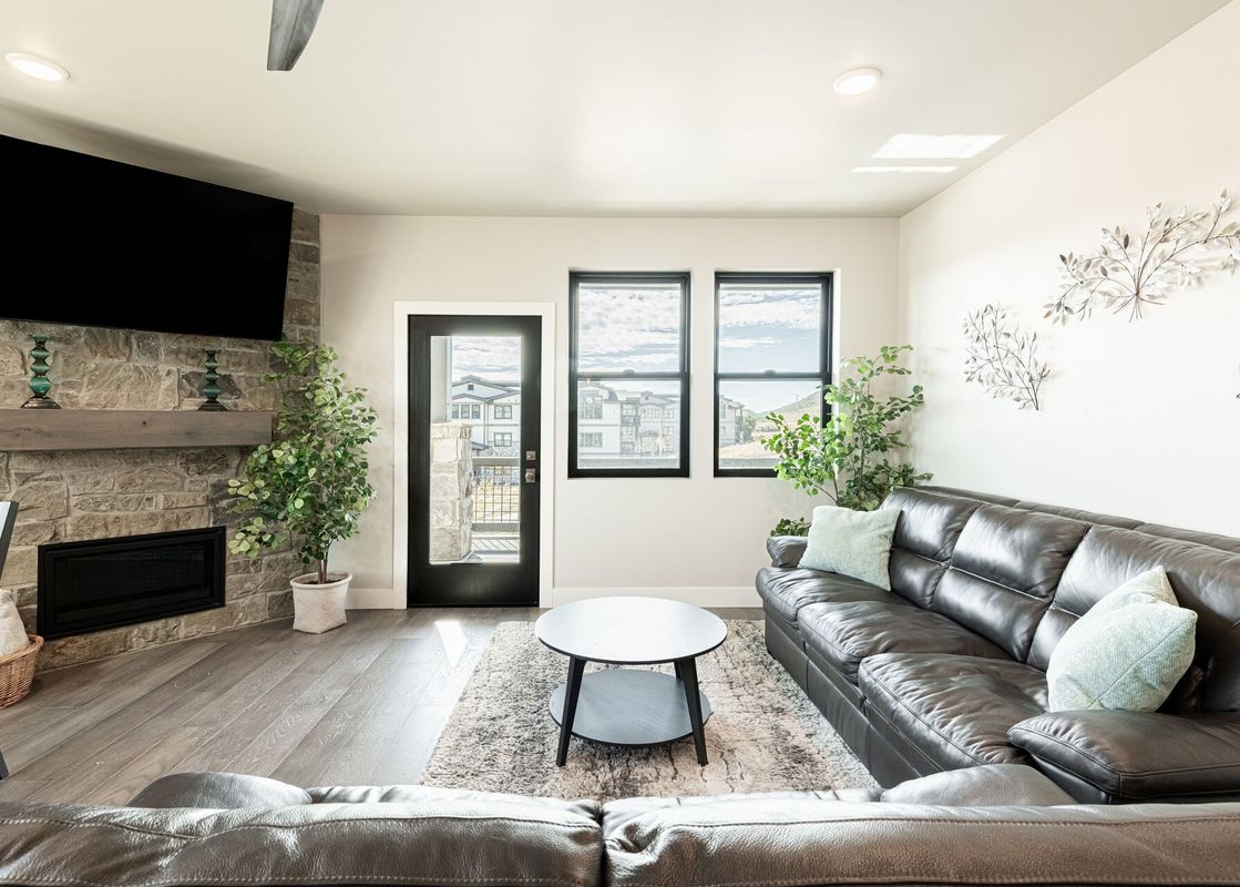 The contemporary living room at Mayflower Lakeside 45-203 with a stone fireplace, leather sectional, and mountain views through the windows.