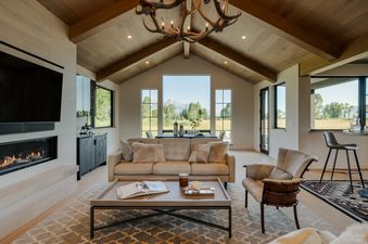 The living room of Oatgrass Escape, showcasing vaulted wooden ceilings, a sleek fireplace, and large windows with scenic outdoor views.