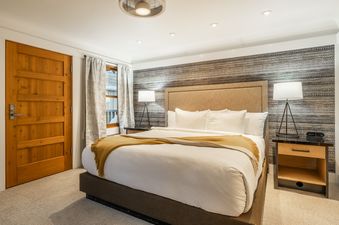 A cozy bedroom in Cedar Crest Osprey Cottage 3 featuring a queen bed with white linens, a golden throw, and modern bedside tables with lamps.