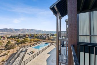 A balcony view of a swimming pool, a residential community, and mountains under a clear blue sky from The Mason 3026.