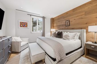 A bright and elegantly furnished master bedroom at Solaris 5F East with a king-sized bed, an accent wooden plank wall, and a window offering a snow-capped mountain view.