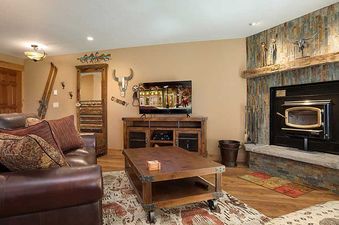 A cozy living room in Ranch at Steamboat RA301 with a leather sofa, a flat-screen TV, a stone fireplace, and rustic decor.