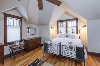 A bedroom with a white bed, a wooden dresser, and a window with a view of trees.