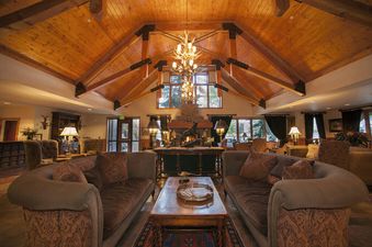 The Hotel Telluride Signature King's grand lobby features vaulted wooden ceilings, a large antler chandelier, and plush seating around a central fireplace, creating a warm and inviting atmosphere for guests.