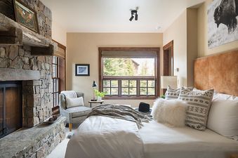 A cozy bedroom in Shooting Star Cabin 02 featuring a plush bed, a stone fireplace, and scenic window views.