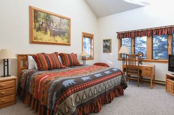 A cozy bedroom in Windriver 1 featuring a bed with a bear-themed comforter and a wooden writing desk near a window.