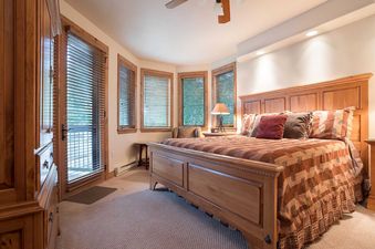 A spacious bedroom in Chateau Chamonix CX336 featuring a large wooden bed with patterned bedding, a bay window with wooden blinds, and a doorway leading outside.