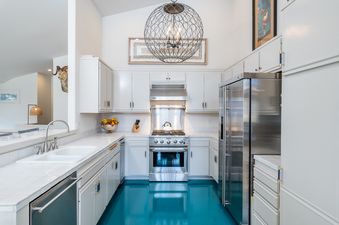 A kitchen with white cabinets, stainless steel appliances, a large chandelier, and a blue floor.