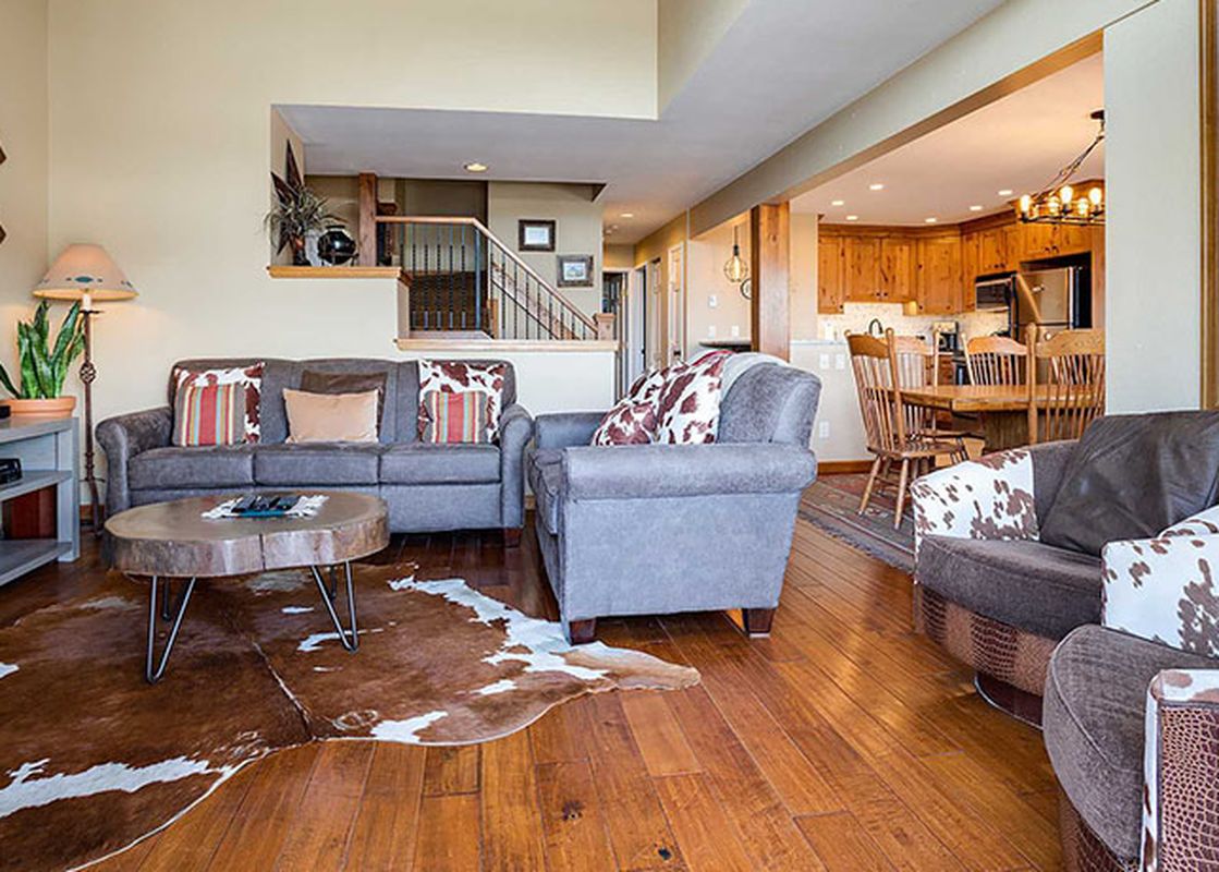 An expansive view of the Ranch at Steamboat RA304's living room and kitchen, featuring a sectional sofa, a tree-slice coffee table, a flat-screen TV, and wooden kitchen cabinetry.