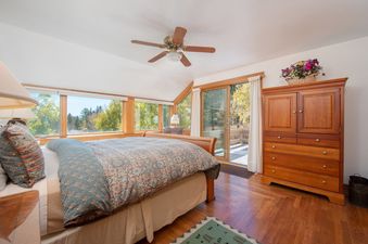 Cozy master bedroom in Barry House with a large bed, wooden armoire, hardwood floors, and large windows looking out to the forest.