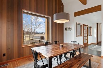 A modern dining area at Columbia Mountain Escape featuring a wooden table with black metal chairs and a bench, set against a wood-paneled wall with a large window overlooking a scenic outdoor view.