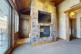A living room with a fireplace, a large window overlooking the outdoors, and a wooden door.