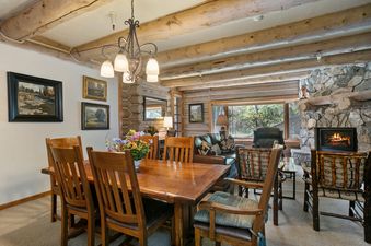 Pine Inn 09 is a charming cabin with a rustic interior. It has a large dining table with chairs and a fireplace in the living room.