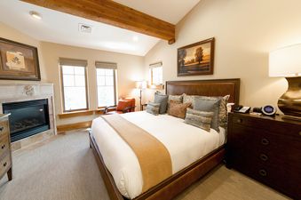 A cozy bedroom with a large bed, fireplace, and two windows, creating a welcoming and comfortable atmosphere.