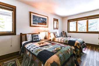 A rustic bedroom in Nez Perce A6 with two twin beds dressed in colorful wilderness quilts under large windows.