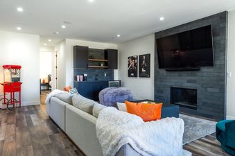 A home theater and wet bar area in Cloud 9 Chalet. The living room has a large sectional sofa, a flat-screen TV, and a fireplace. The wet bar features dark cabinets, a sink, and a popcorn machine.