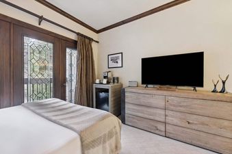 A serene guest bedroom at The Charter C115 features a comfortable bed, a glass door to a balcony, a television, and a coffee maker.