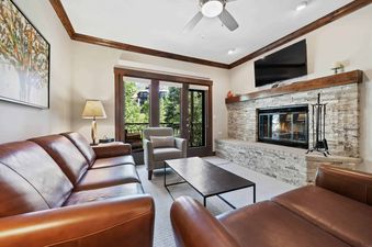 A cozy living room at The Charter C2305 with leather sofas, a stone fireplace, and a balcony with a view of trees.